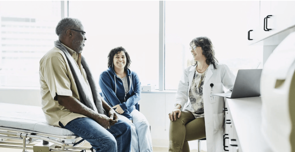 Smiling female doctor consulting with senior male patient and adult daughter in exam room