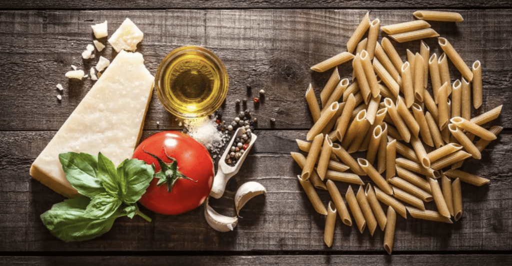 Whole grain penne, olive oil, tomato, basil and feta cheese, garlic on a wooden board.